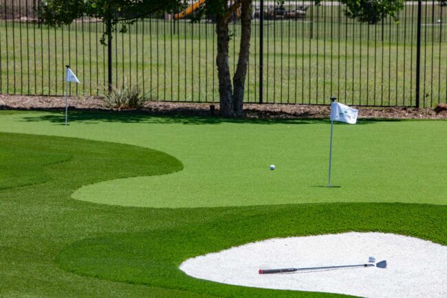 Residential backyard putting green with artificial turf, sand bunker, and golf accessories—perfect inspiration for backyard putting green ideas in Utah.