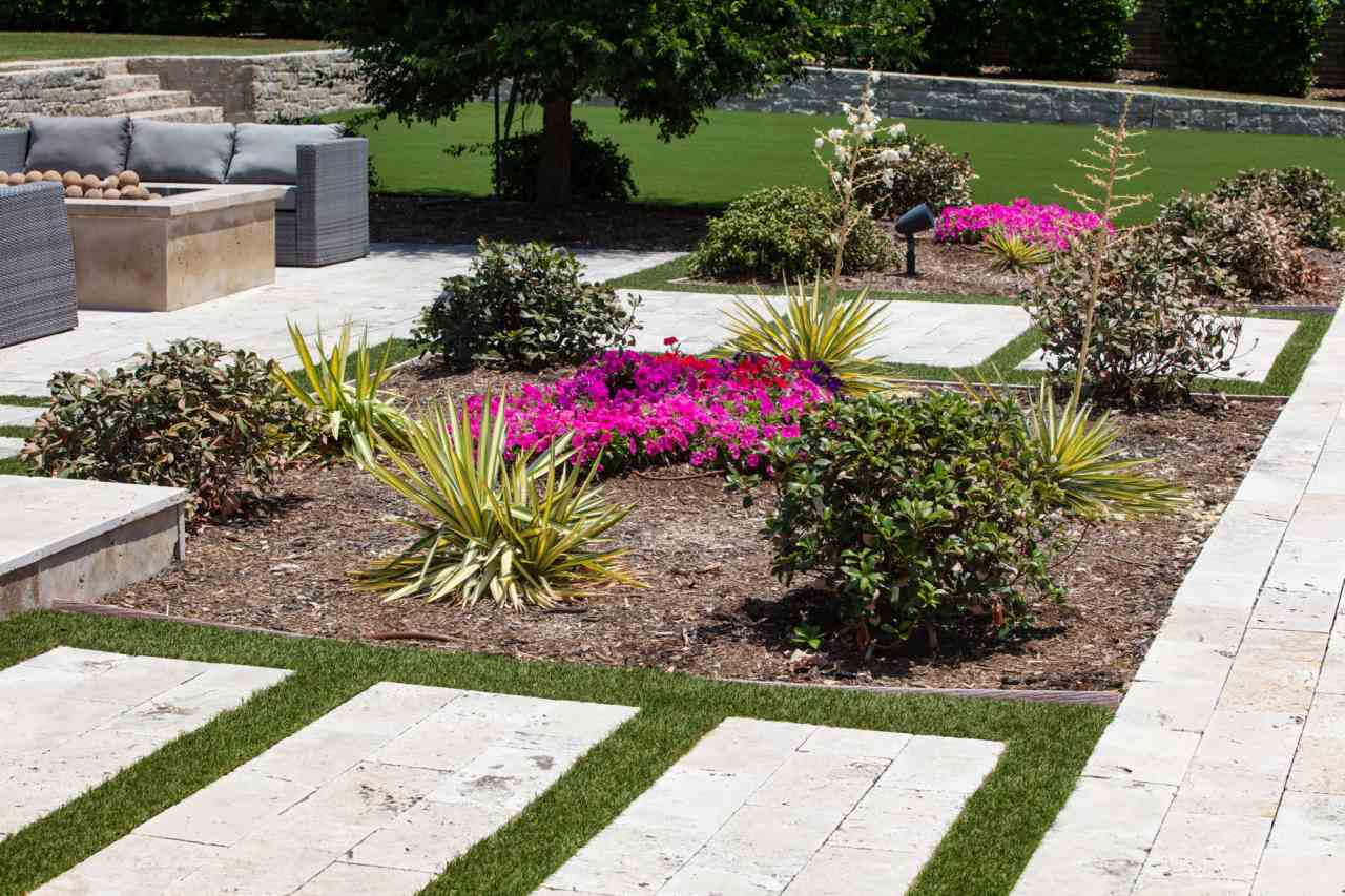 Low-water landscape with bright pink flowers, drought-tolerant plants, pavers, and artificial grass in a modern backyard.