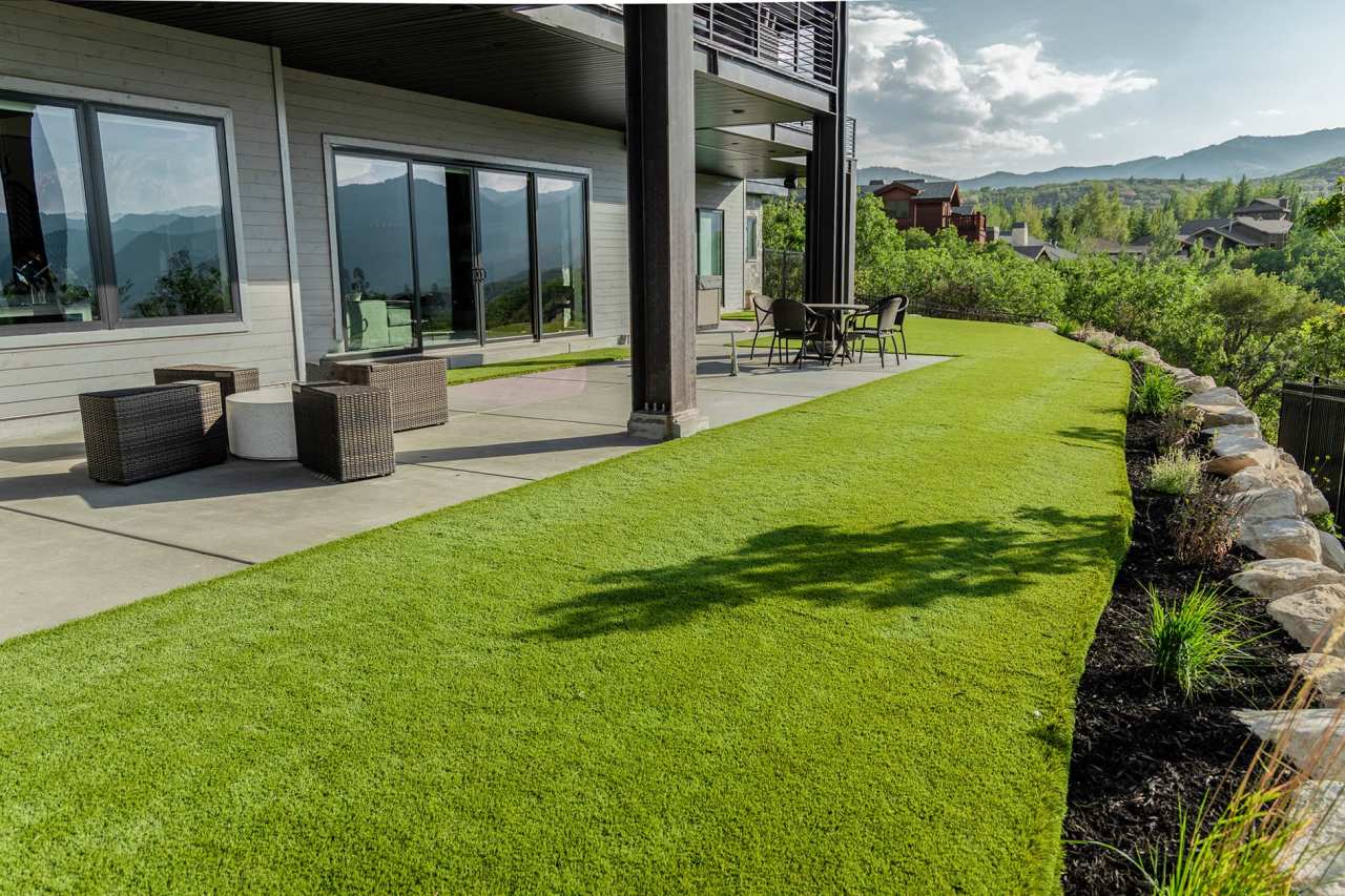 A modern home with a scenic mountain view features a backyard of artificial turf and a shaded concrete patio.